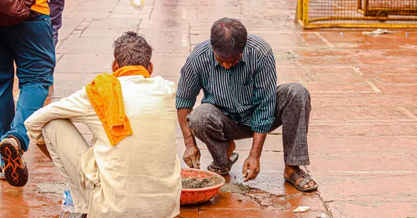 Two workers repairing a street with red floor tiles, surrounded by people in urban setting. men repairing the floor tiles