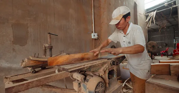 A carpenter in a dusty workshop precisely cuts wood using an industrial saw. carpenter working with wood on industrial saw