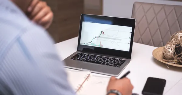 A person analyzes cryptocurrency data on a laptop during remote work from a home office. gray laptop on table top