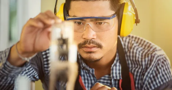 Carpenter wearing protection gear measuring wood in a workshop with great focus and precision. focused carpenter measuring wood with precision