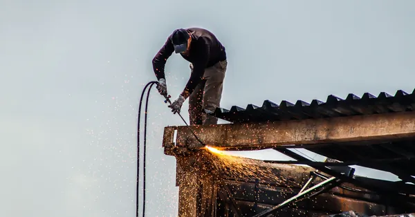 A worker cutting metal on a roof with visible sparks during construction work. a man working on the roof