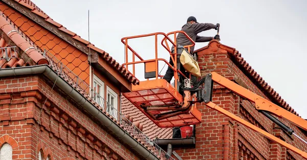 Roofer in a cherry picker conducting maintenance on a red brick building with a tiled roof. roofer performing maintenance on red brick building