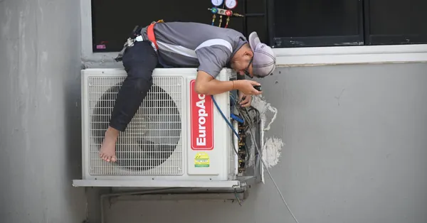 A technician skillfully repairing an outdoor air conditioning unit mounted on a building wall. man in gray t shirt fixing the aircon